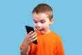 A little boy looks at the phone, and is surprised. Isolated on a blue background Royalty Free Stock Photo