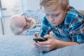 Little boy lying on bed and using his smartphone while his granpa is napping