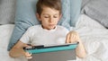 A little boy is lying on his bed and playing with a tablet computer during the day. Child using gadget, education and development Royalty Free Stock Photo
