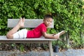 Little boy lying on the wooden bench hand holding a book looking Royalty Free Stock Photo