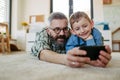 Little boy making selfie on smartphone with father, lying on floor in kids room, making silly faces. Dad explaining Royalty Free Stock Photo