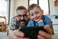 Little boy making selfie on smartphone with father, lying on floor in kids room, making silly faces. Dad explaining Royalty Free Stock Photo