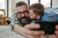 Little boy making selfie on smartphone with father, lying on floor in kids room, making silly faces. Dad explaining Royalty Free Stock Photo