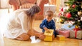 Cute little boy with mother sitting under Christmas tree and open gift box Royalty Free Stock Photo