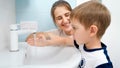 Little boy with mother washing his mouth and face with water and wiping with blue towel. Concept of hygiene and Royalty Free Stock Photo