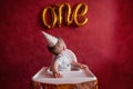 Little boy of one year in festive hat sits in children`s chair, looks at the foil gold balloons One Royalty Free Stock Photo