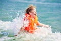 Little boy in orange life vest swimming in wave sea