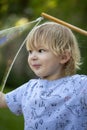 Young, 4 year old preschool boy with a grey shirt and blond hair, blowing bubbles in the yard Royalty Free Stock Photo