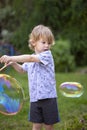 Young, 4 year old preschool boy with a grey shirt and blond hair, blowing bubbles in the yard Royalty Free Stock Photo