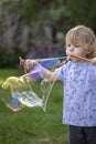 Young, 4 year old preschool boy with a grey shirt and blond hair, blowing bubbles in the yard Royalty Free Stock Photo