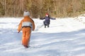 The little boy in overalls running through the snow toward the mother. Winter day in the coniferous forest. Back view