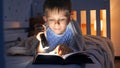 Little boy in pajamas lying in bed and reading bedtime story book with torch. Children education, development, secrecy, privacy, Royalty Free Stock Photo