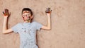 Little boy with palms and face in bright colorful paints looking at camera lying on floor Royalty Free Stock Photo