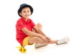 A little boy in panama, yellow jersey, red shorts and white sneakers sits on a yellow penny and smiles