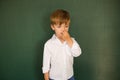 Little boy picks his nose near the blackboard and does not know the answer to the school assignment