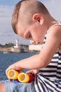 Little boy playing with binoculars on the background of the sea and lighthouse