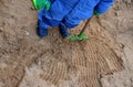 Little boy playing in blue winter overalls and green fingerless gloves on the sandpit. He holds habits and digs sand. There is a w Royalty Free Stock Photo