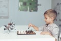 A little boy is playing chess with a gray robot. Robot plays for whites