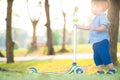 Little boy playing child scooter in city prak on green meadow