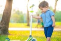 Little boy playing child scooter in city prak on green meadow