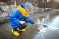 Little boy playing with paper boat in large puddle near town houses in early spring. Paper ship floating in water Royalty Free Stock Photo