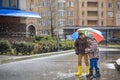 Little boy playing in rainy summer park. Child with colorful rainbow umbrella, waterproof coat and boots jumping in puddle and mud Royalty Free Stock Photo