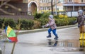 Little boy playing in rainy summer park. Child with colorful rainbow umbrella, waterproof coat and boots jumping in puddle and mud Royalty Free Stock Photo