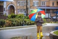 Little boy playing in rainy summer park. Child with colorful rainbow umbrella, waterproof coat and boots jumping in puddle and mud Royalty Free Stock Photo