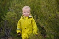 Little boy playing in rainy summer park. Child with colorful rainbow umbrella, waterproof coat and boots jumping in Royalty Free Stock Photo