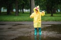 Little boy playing in rainy summer park. Child with umbrella, waterproof coat and boots jumping in puddle and mud in the rain. Kid Royalty Free Stock Photo