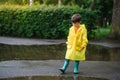 Little boy playing in rainy summer park. Child with umbrella, waterproof coat and boots jumping in puddle and mud in the rain. Kid Royalty Free Stock Photo