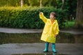 Little boy playing in rainy summer park. Child with umbrella, waterproof coat and boots jumping in puddle and mud in the rain. Kid Royalty Free Stock Photo