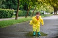 Little boy playing in rainy summer park. Child with umbrella, waterproof coat and boots jumping in puddle and mud in the rain. Kid Royalty Free Stock Photo