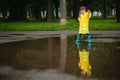 Little boy playing in rainy summer park. Child with umbrella, waterproof coat and boots jumping in puddle and mud in the rain. Kid Royalty Free Stock Photo