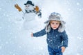Little boy playing with snowman in winter park. Winter portrait of cute child in snow Garden. People in snow. Happy