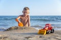 A little boy plays with sand and toys on the beach near the sea Royalty Free Stock Photo