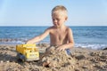 A little boy plays with sand and toys on the beach near the sea Royalty Free Stock Photo