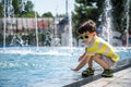 Little boy plays in the square near pool with water jets in the fountain at sunny summer day. Active summer leisure for kids in Royalty Free Stock Photo