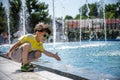 Little boy plays in the square near pool with water jets in the fountain at sunny summer day. Active summer leisure for kids in Royalty Free Stock Photo