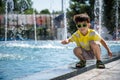 Little boy plays in the square near pool with water jets in the fountain at sunny summer day. Active summer leisure for kids in Royalty Free Stock Photo