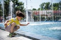 Little boy plays in the square near pool with water jets in the fountain at sunny summer day. Active summer leisure for kids in Royalty Free Stock Photo