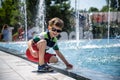 Little boy plays in the square near pool with water jets in the fountain at sunny summer day. Active summer leisure for kids in Royalty Free Stock Photo