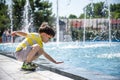 Little boy plays in the square near pool with water jets in the fountain at sunny summer day. Active summer leisure for kids in Royalty Free Stock Photo