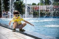 Little boy plays in the square near pool with water jets in the fountain at sunny summer day. Active summer leisure for kids in Royalty Free Stock Photo