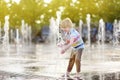 Little boy plays in the square between the water jets in the fountain at sunny summer day Royalty Free Stock Photo