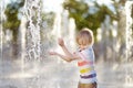 Little boy plays in the square between the water jets in the fountain at sunny summer day Royalty Free Stock Photo