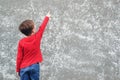 Little boy pointing on empty place at concrete wall. Back view of child. Cool boy wearing red shirt and jeans. Mockup. Child is Royalty Free Stock Photo