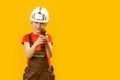 Little boy pretends to drill wall with drill against yellow isolated background. Boy teenager as builder worker. Copy space,