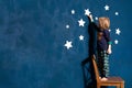 Little boy in pyjamas decorate blue bedroom wall with white paper stars.