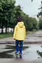 Little boy in raincoat and rubber boots playing in puddle. Fun on street.